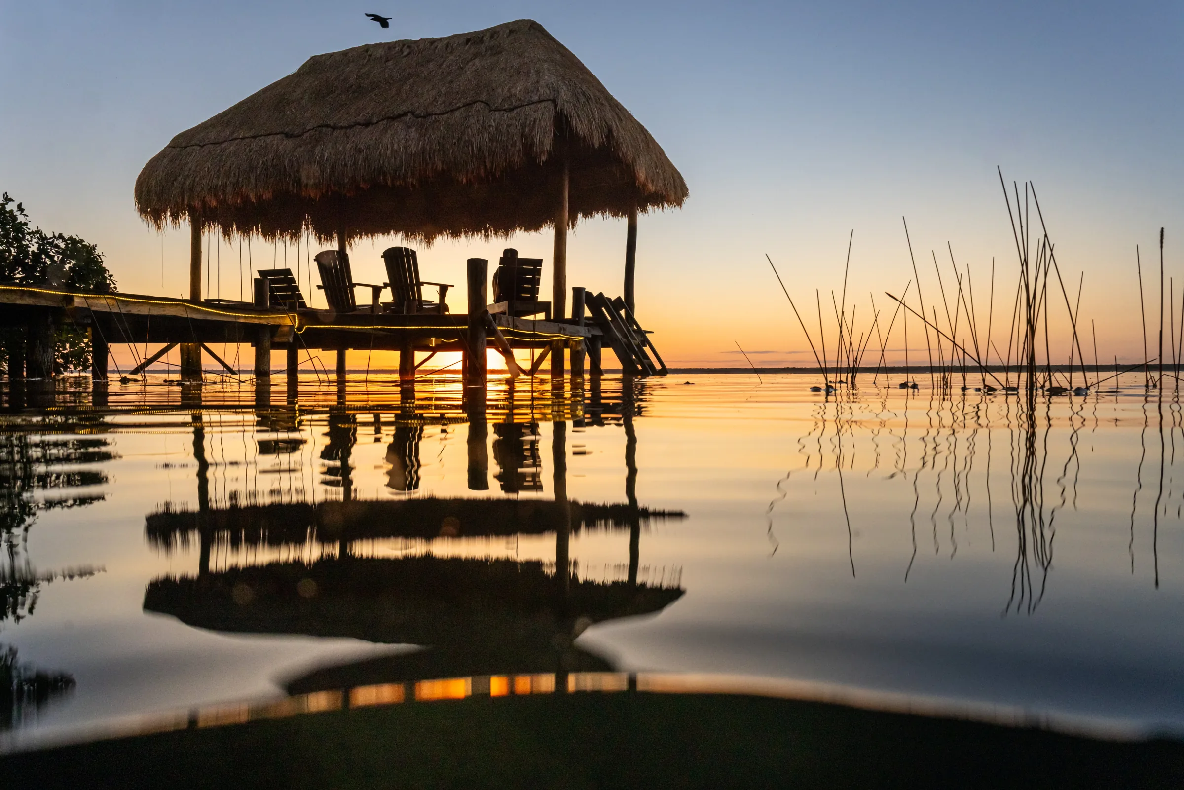 Sunrise over Bacalar lagoon, with Villa Alegre's dock and palapa reflected in the still water